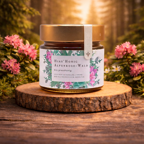 Bio Alpenrose-Wald Honig Presshonig aus Österreich im Glas auf Holzscheibe, umgeben von Alpenrosen im warmen Abendlicht, Premium Honig online kaufen